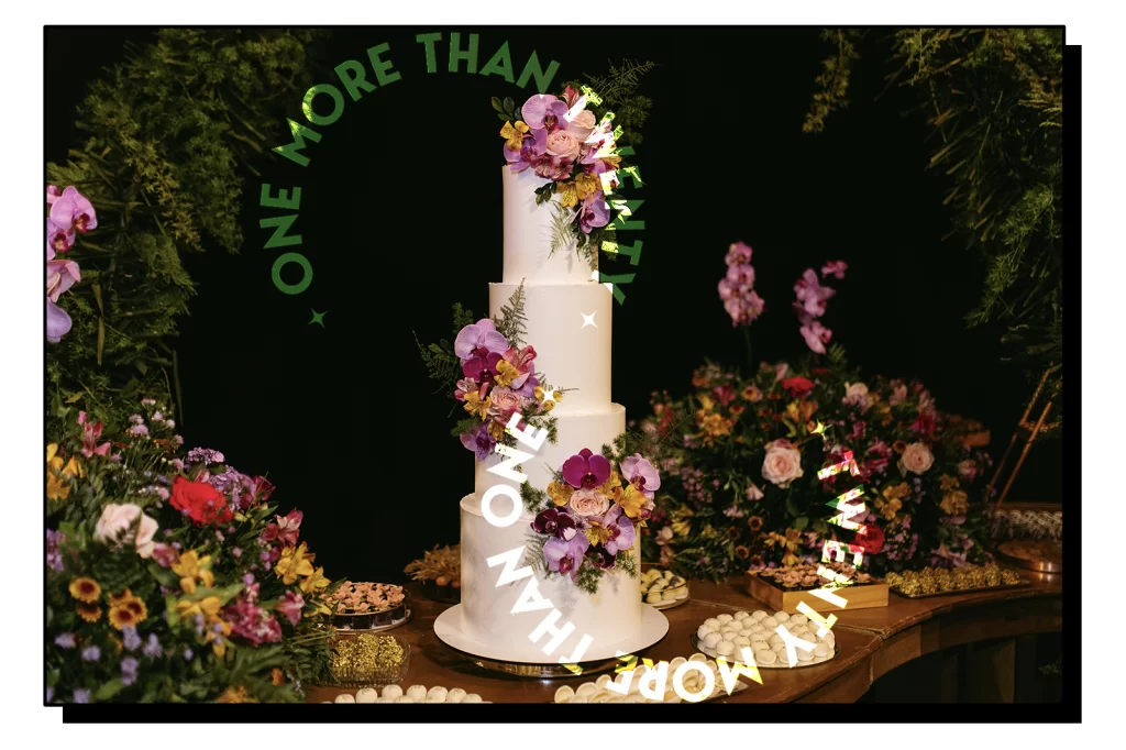 A wedding cake placed on a table, decorated with some flower bouquet and accompanied by some sweets